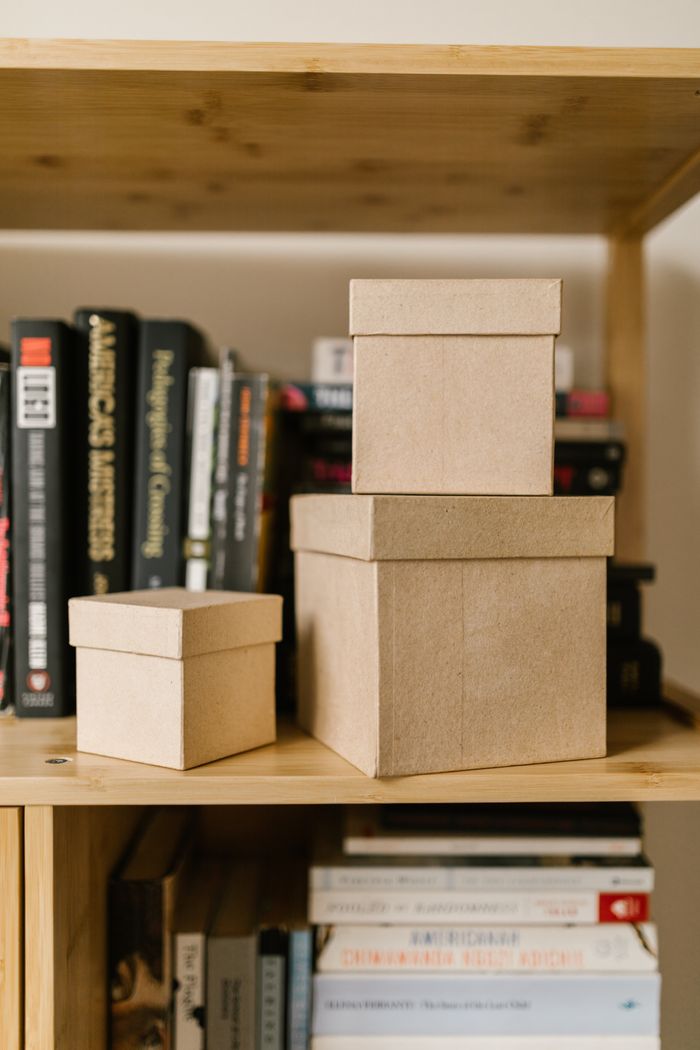 project-01-c Close-up of cardboard boxes on a wooden bookshelf surrounded by various books.